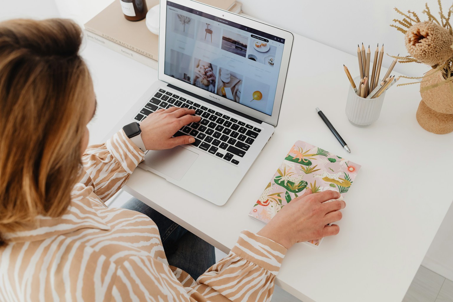 A woman planning at a laptop with a notebook in a bright home workspace